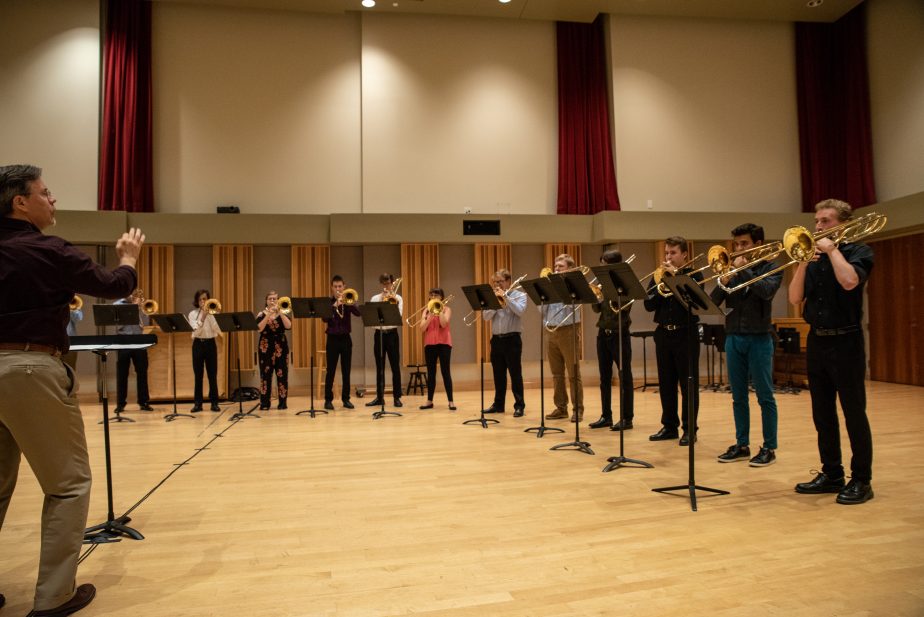 Trombone Institute participants with trombones and music stands rehearsing with instructor in Ray Wright Room