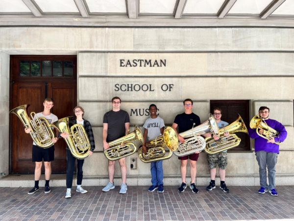 7 students holding tubas in a line in front of Eastman School of Music 