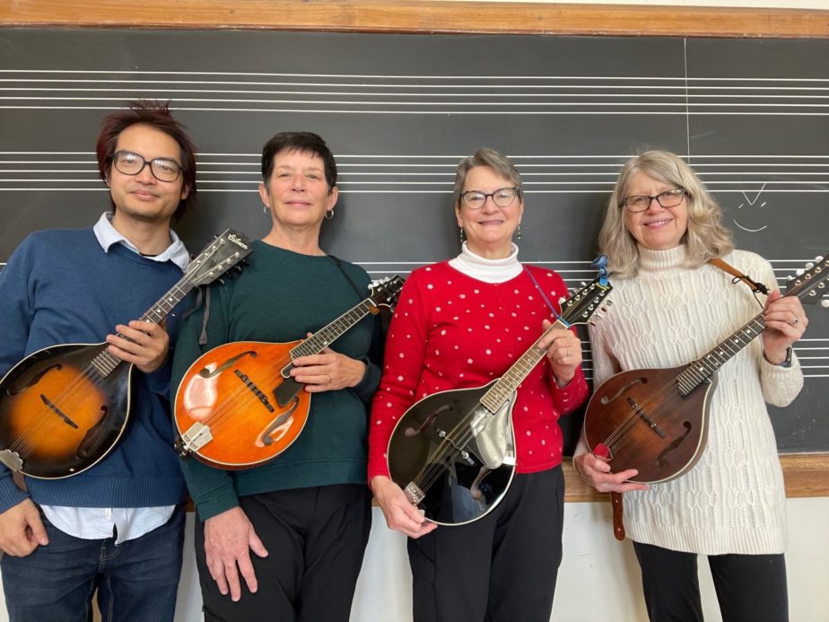 Four mandolin students holding mandolins in front of chalkboard