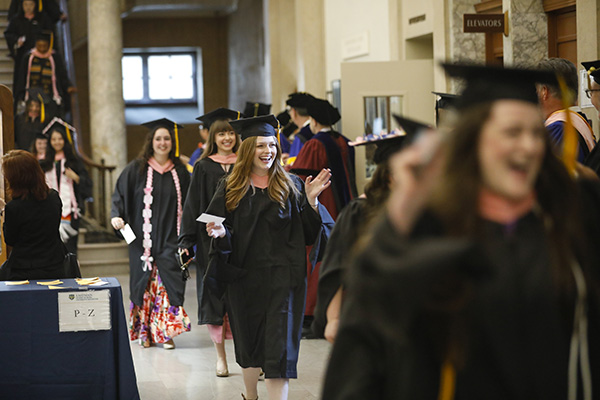 Eastman Student smiling and waving during commencement in Lowry Hall
