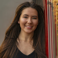 pictured: Lindsay Haukom, a woman with brown hair smiles next to a harp